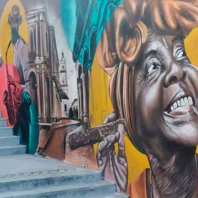 Graffiti de una señora cubana con turbante fumando un puro, una calle de Cuba y un músico de jazz tocando el saxofón