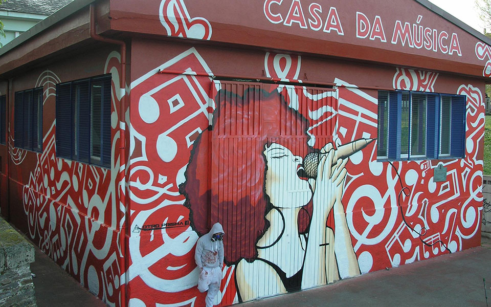 Diego AS posa junto al graffiti de una mujer cantando con notas musicales de fondo