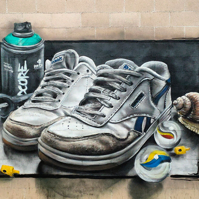 Graffiti en un muro de unas zapatillas, un bote de spray, canicas y un caracol